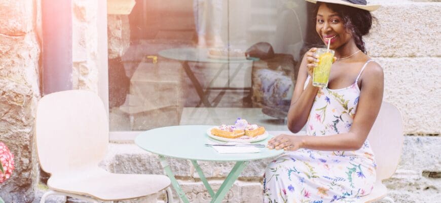 A woman sitting at an outdoor cafe table, sipping a drink with food in front of her