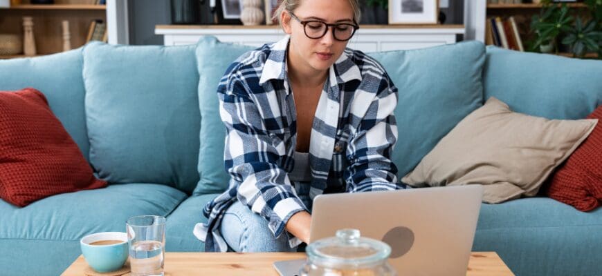 A woman sitting on a couch in a living room and working on a laptop